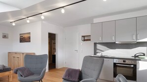 A modern kitchen with grey cabinets, a built-in oven, and a dining area with grey upholstered chairs.