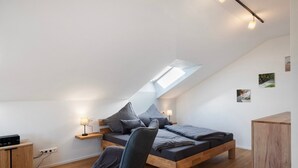 A modern bedroom with a sloped ceiling, a bed with grey bedding, a wooden nightstand, a desk, and a chair.