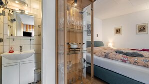 Een slaapkamer met een bed, nachtkastje, spiegel, garderobe en een glazen kast met wijnglazen.