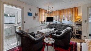 Een woonkamer met een bank, een klein tafeltje, een televisie en een raam met gordijnen.
