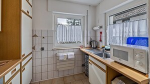 Een kleine keuken met een magnetron, spoelbak en raam met gordijnen.