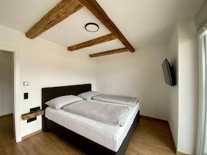 A bedroom with a bed, wooden beams, a wall-mounted TV, and a door.