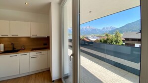 A modern kitchen with white cabinets and a wooden countertop, a large window with a view of mountains and buildings.