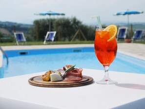 A poolside table with a drink and food, surrounded by lounge chairs and umbrellas.