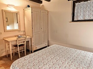 A bedroom with a bed, a desk with a chair, a wardrobe, a mirror, and a window with curtains.