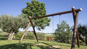 Ein hölzernes Schaukelgerüst in einem grünen Park mit Bäumen und einem Zaun im Hintergrund.