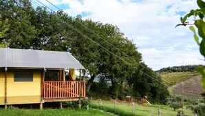 A yellow cabin with a wooden deck and a covered porch, surrounded by lush greenery and a hilly landscape. - Studio in Marche With Pool Near Adriatic (Lapedona)
