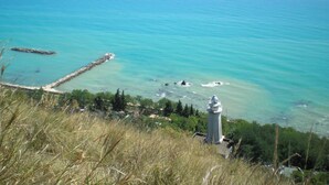 A coastal landscape with a lighthouse, clear blue sea, rocky outcrops, and grassy terrain. - Studio in Marche With Pool Near Adriatic (Lapedona)