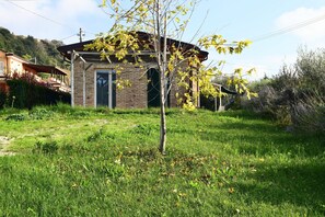 Standalone cottage with a welcoming arched doorway and porch, set amidst lush green surroundings.