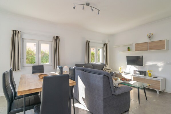A modern living room with a sofa, dining table, chairs, and a TV.