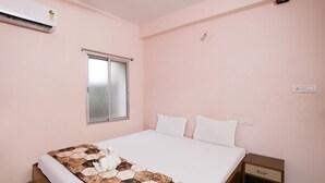 A bedroom with a bed, a nightstand, a window, and an air conditioner. - Hotel Shivangi Eco TripandTrip (Puri)