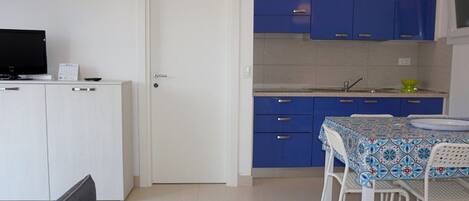 Uma cozinha compacta com armários azuis, uma porta branca e um espaço de refeições com mesa e cadeiras.
