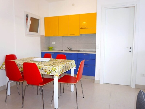 Een compacte keuken met gele kastjes, een witte deur en een eettafel met rode stoelen.