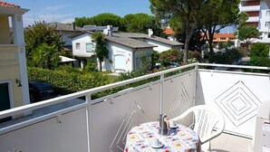Un balcon avec une table et des chaises, donnant sur un quartier résidentiel avec des maisons et des arbres.