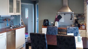 Een compacte keuken met witte kasten, een roestvrijstalen afzuigkap en een eethoek met gestreept beklede stoelen.