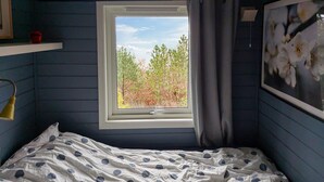 Een slaapkamer met een enkel bed, een raam met uitzicht op bomen en een schilderij aan de muur.
