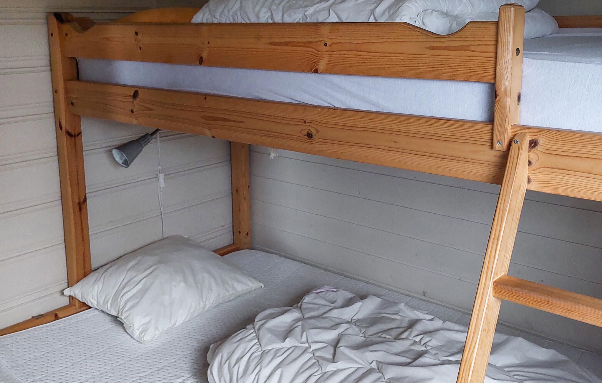 A bunk bed with a wooden frame, white bedding, and a single pillow.