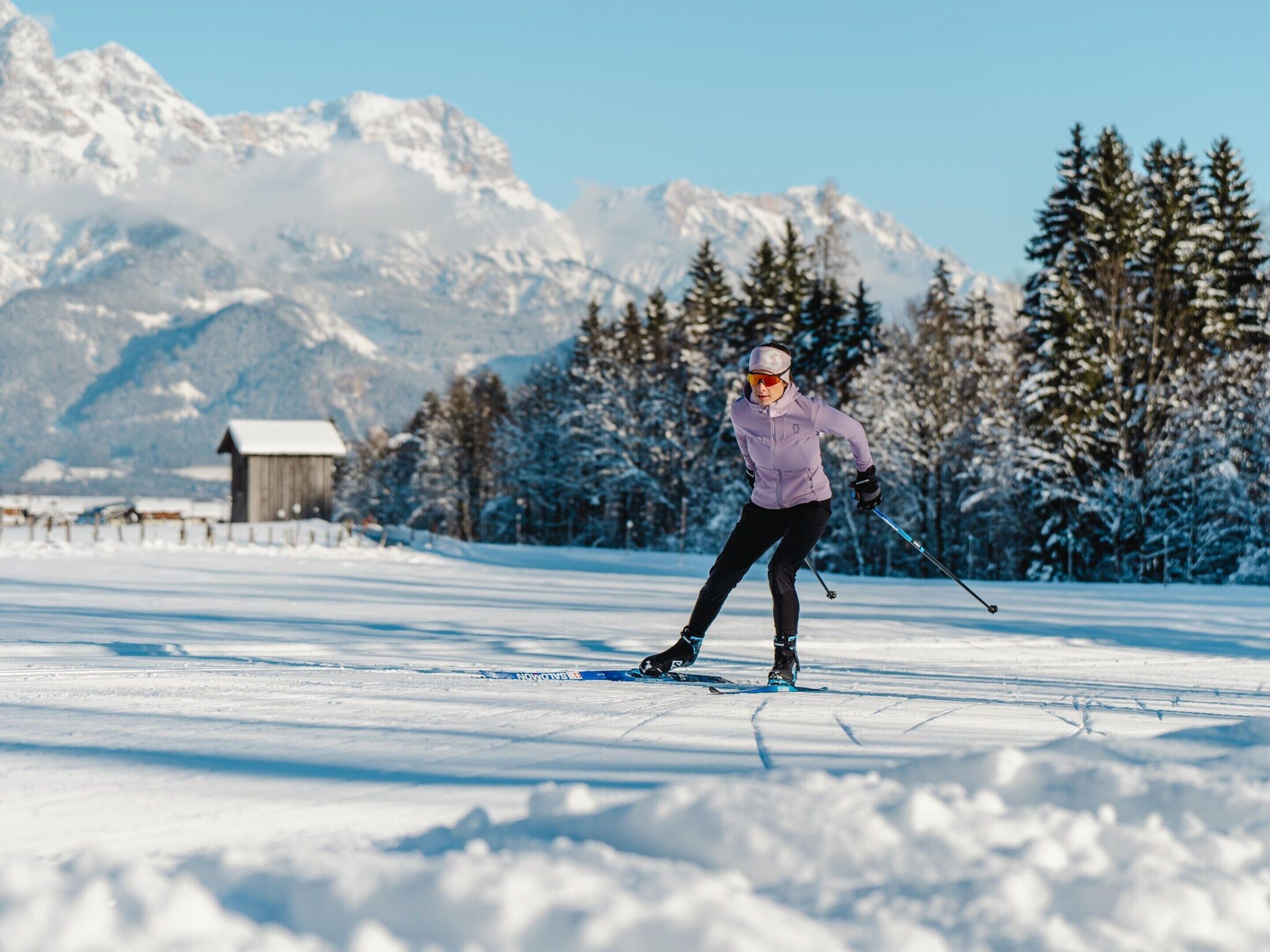 Une personne pratiquant le ski de fond dans un paysage enneigé, avec une montagne en arrière-plan.