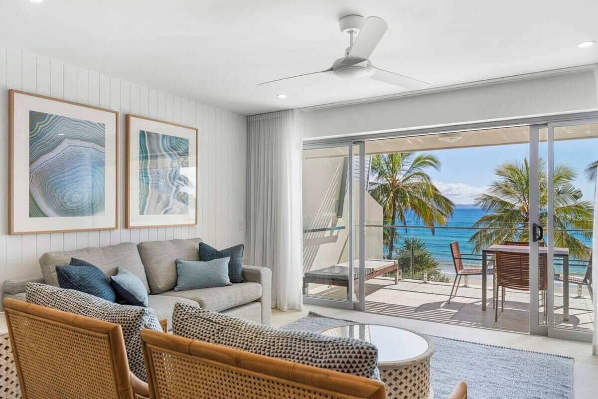 A modern living room with a sofa, chairs, and a view of the ocean through large glass doors.