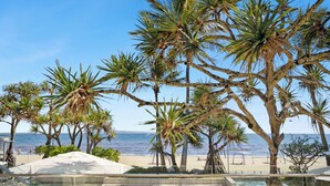 Zwembadgedeelte met helder water, omringd door palmbomen en een strand op de achtergrond.