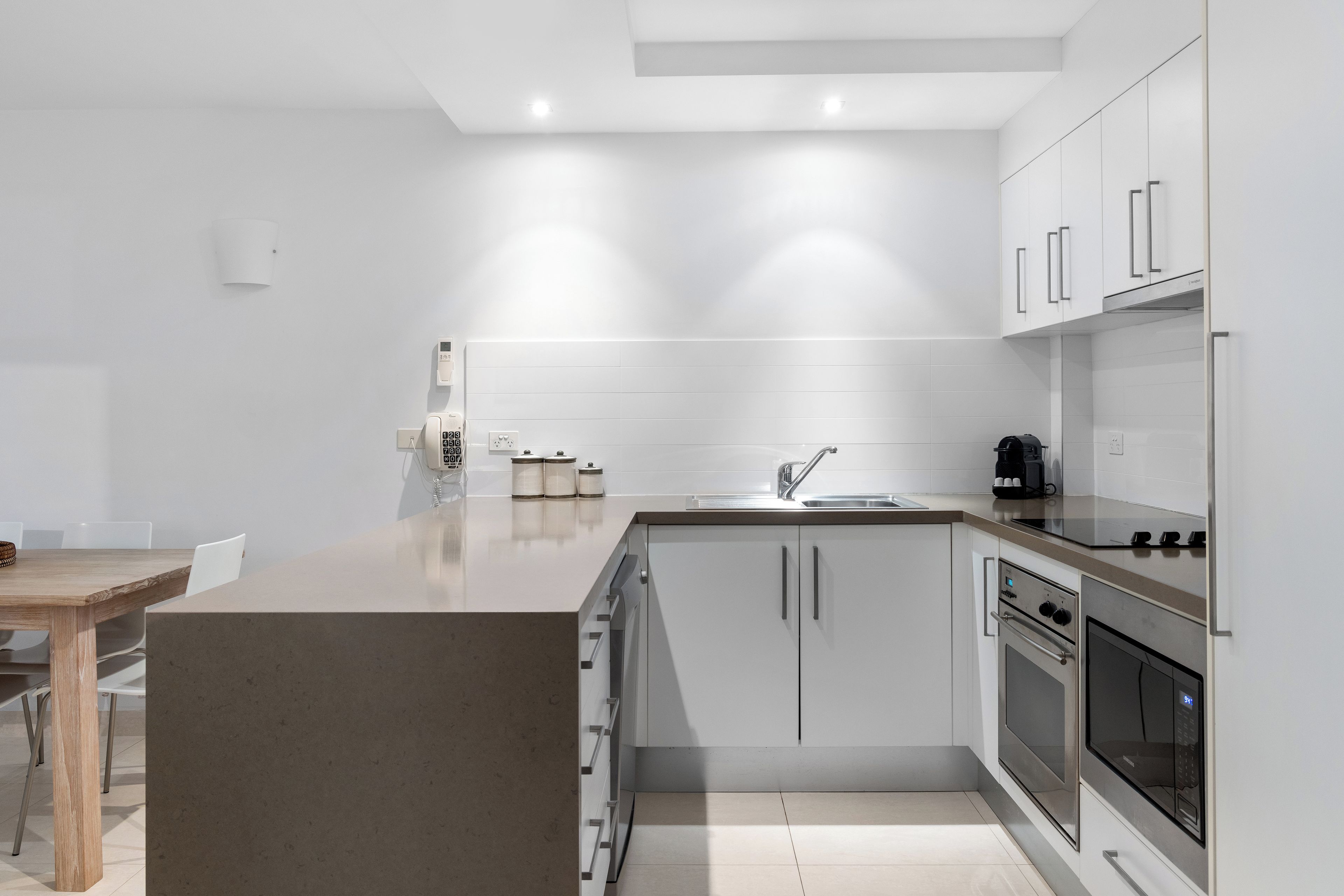 Una cocina moderna con armarios blancos, horno empotrado, microondas y cafetera.