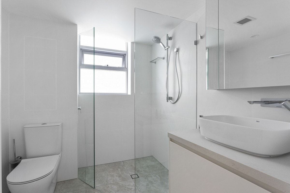A modern bathroom with a glass-enclosed shower, a toilet, and a sink with a mirror above.