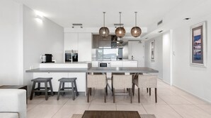 Een moderne keuken met een groot schiereiland, barstoelen, hanglampen en uitzicht op de woonkamer.