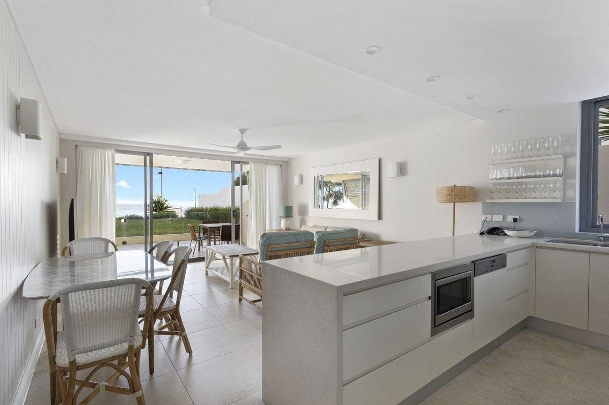 A modern kitchen with a central island, dining area with wicker chairs, and a view of the outdoors.