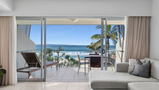 Een moderne woonkamer met een grote schuifpui die leidt naar een balkon met uitzicht op zee.