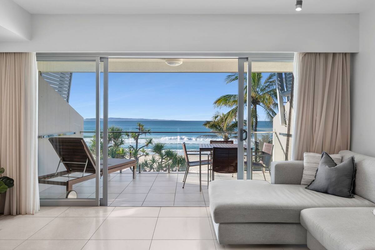 A modern living room with a large sliding glass door leading to a balcony with a view of the ocean.