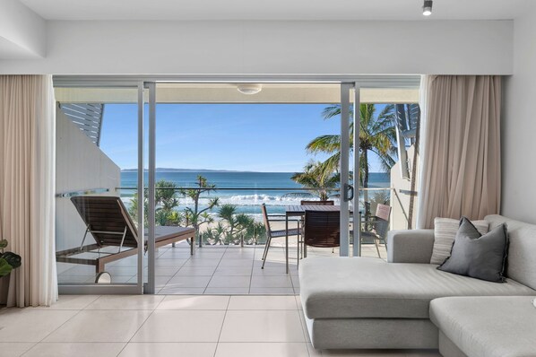 A modern living room with a large sliding glass door leading to a balcony with a view of the ocean.