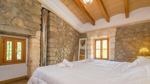 A bedroom with a stone wall, wooden beams, a large bed, and a fireplace. - Son Paparra - Villa With Private Pool In Inca (Inca, Illes Balears)