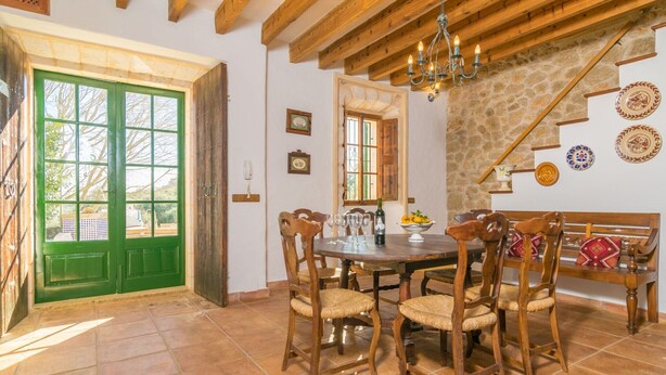 A dining area with a wooden table, chairs, and a bench. There is a green door, a stone wall, and a chandelier. - Son Paparra - Villa With Private Pool In Inca (Inca, Illes Balears)