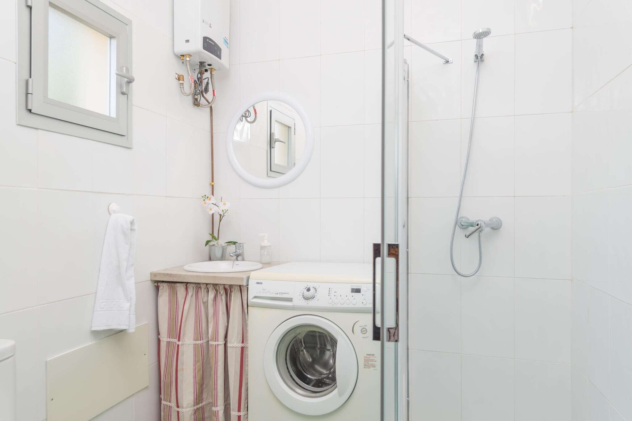 A compact bathroom with a washing machine, a shower, a toilet, and a small sink with a mirror.