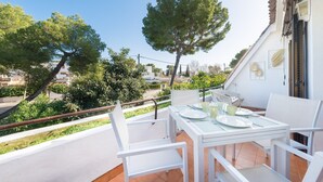 Un balcón con mesa lista para dos personas, sillas y vistas a la vegetación y edificios circundantes.