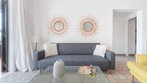 Una sala de estar con un sofá gris, dos espejos en la pared, una mesa de centro de vidrio y un sillón amarillo.