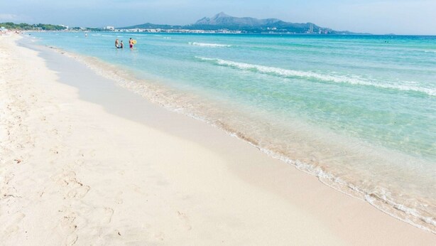Una playa con aguas turquesas cristalinas, una orilla arenosa y una montaña al fondo.