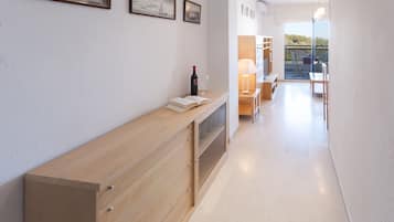 Un corridoio con una consolle in legno, un libro e una bottiglia di vino. Alle pareti, quadri incorniciati e una vista su un balcone con mobili da esterno.