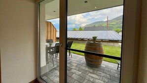 A room with a large sliding glass door leading to an outdoor patio with a wooden table, chairs, and a large barrel. - Apartment in Saalfelden Near Ski Slopes (Saalfelden am Steinernen Meer)
