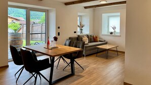 A modern living room with a wooden dining table, black chairs, a grey sofa, and a wooden ceiling beam. - Apartment in Saalfelden Near Ski Slopes (Saalfelden am Steinernen Meer)