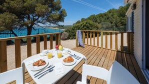 Una terrazza in legno con un tavolo apparecchiato per la colazione, con vista su una spiaggia e alberi.