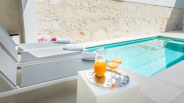 A poolside area with lounge chairs, a table with a pitcher of orange juice and two glasses, and a stone wall in the background. - Ca Na Foc - Villa With Private Pool In Sa Pobla (Sa Pobla, Illes Balears)