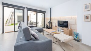 A modern living room with a grey sofa, a wooden coffee table, and a television. There is a fireplace and a balcony visible through the glass doors. - Ca Na Foc - Villa With Private Pool In Sa Pobla (Sa Pobla, Illes Balears)