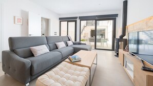 A modern living room with a grey sectional sofa, a wooden coffee table, and a beige ottoman. A flat-screen TV is mounted on a wooden cabinet, and a fireplace is visible in the background. - Ca Na Foc - Villa With Private Pool In Sa Pobla (Sa Pobla, Illes Balears)