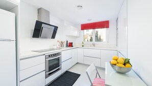 Une cuisine moderne avec des meubles blancs, un four en acier inoxydable, un micro-ondes noir et une fenêtre avec des stores rouges.