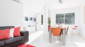 Un salon moderne avec un canapé noir, des coussins rouges et un tapis rouge. On y trouve également un coin repas avec une table et des chaises, ainsi qu’une grande fenêtre donnant sur un paysage verdoyant.