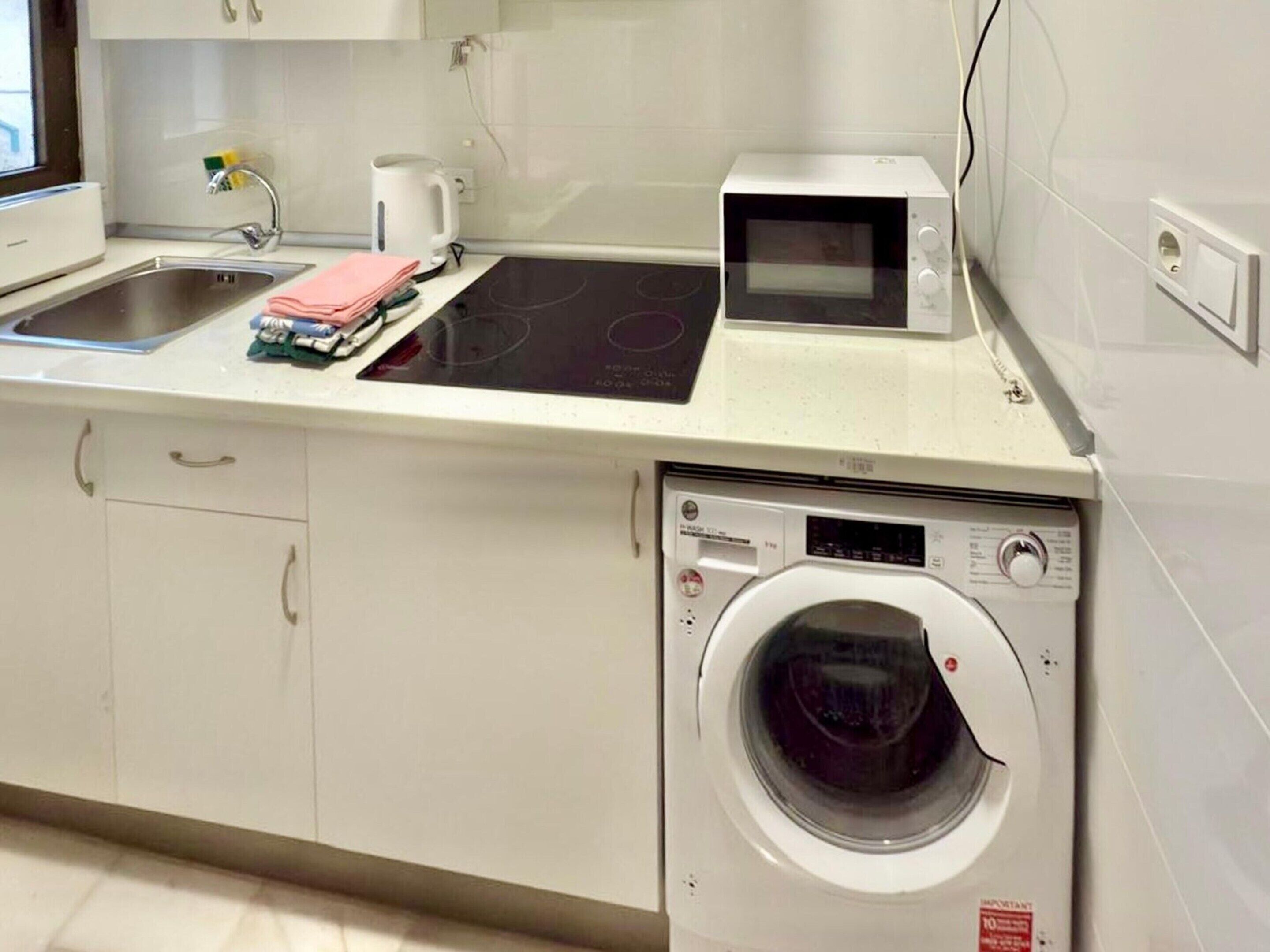 A compact kitchen with a built-in washer and dryer, a microwave, and a sink.