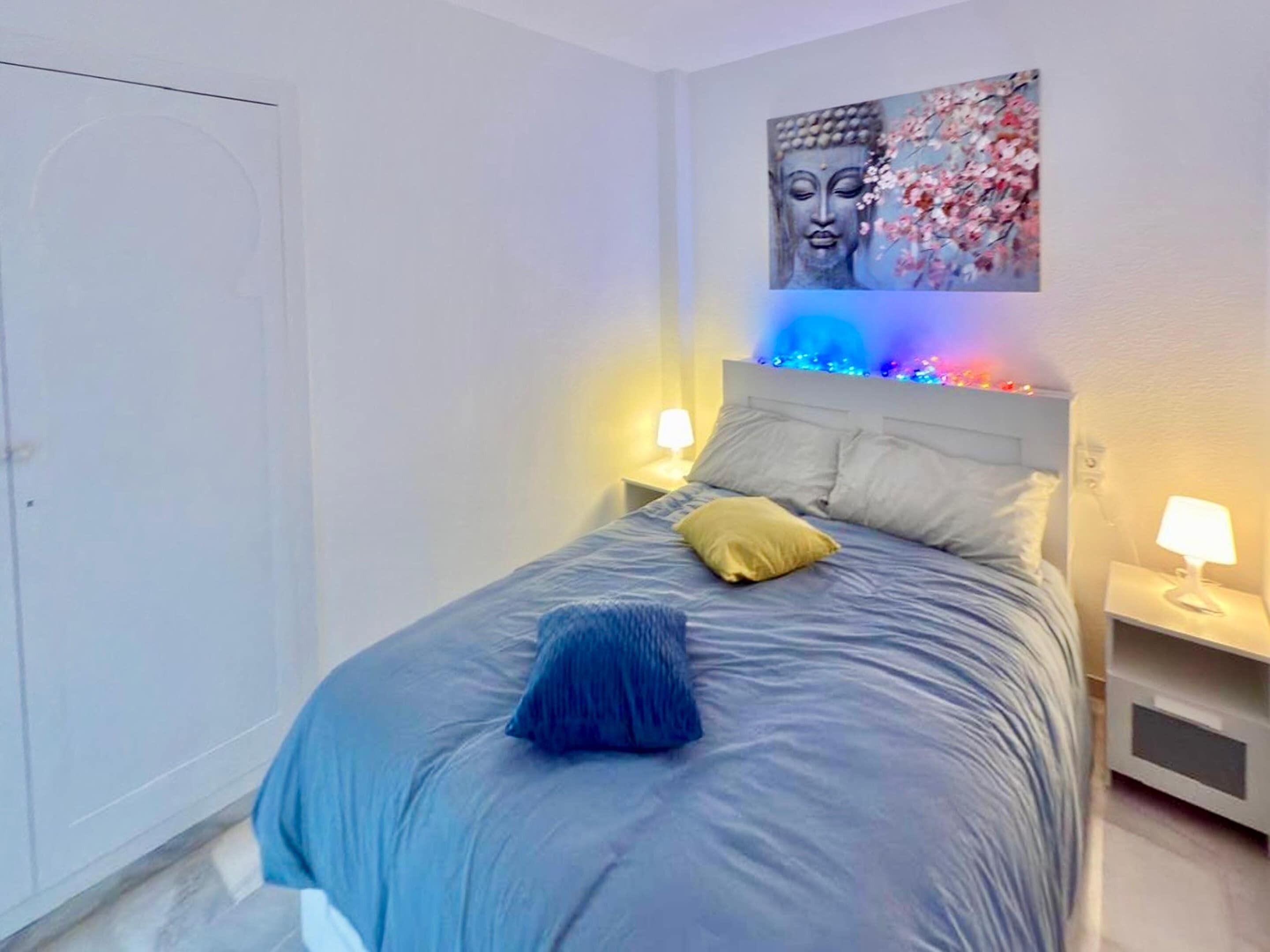 Ein Schlafzimmer mit Bett, Kissen, Nachttisch, Wandbild und einer Tür.