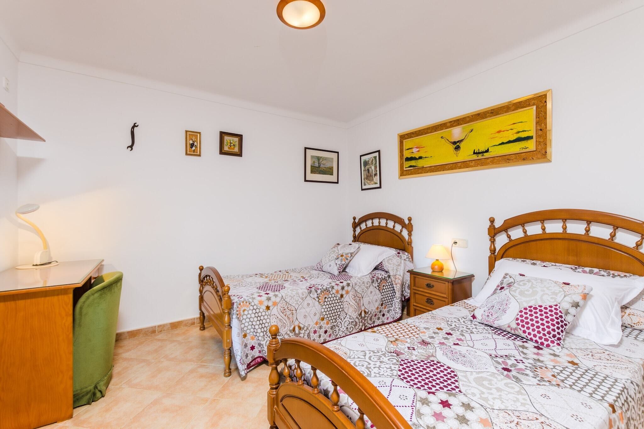 A bedroom with two wooden beds, a desk, and a chair.