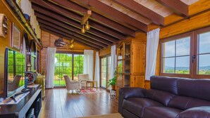 A cozy living room with a leather sofa, wooden flooring, and large windows offering a view of the outdoors.